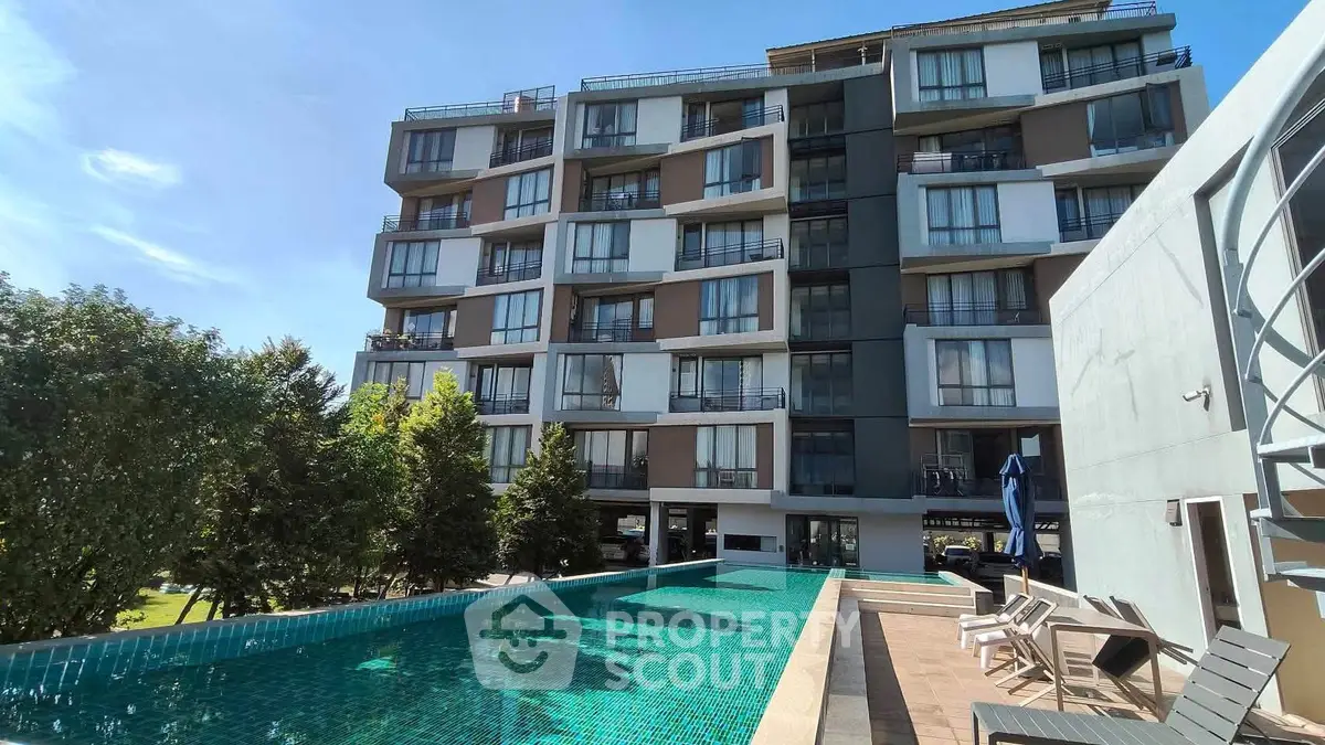Modern apartment building with pool and sun loungers, ideal for luxury living.