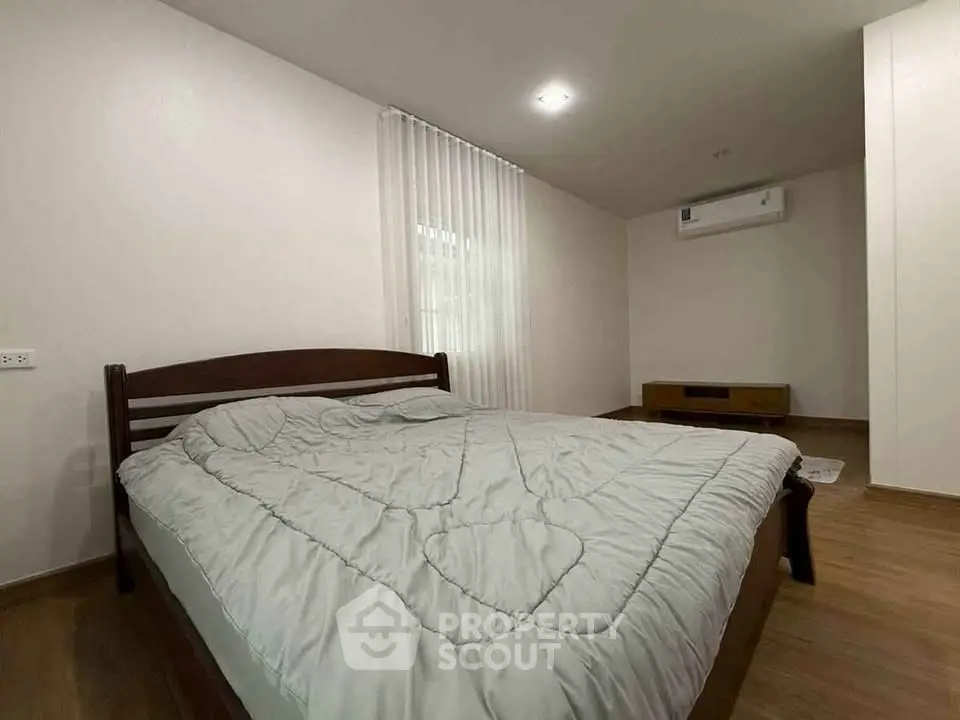 Cozy bedroom with wooden flooring and modern air conditioning unit, perfect for restful nights.