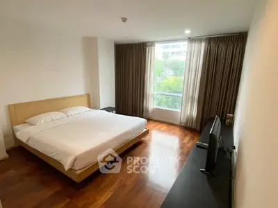 Spacious bedroom with large window and wooden flooring in modern apartment.