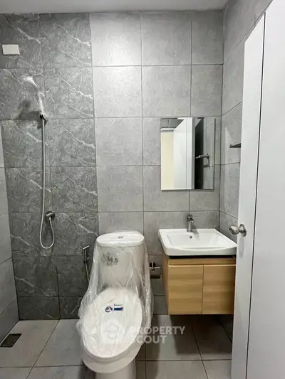Modern bathroom with sleek gray tiles, wall-mounted sink, and shower area in a contemporary apartment.
