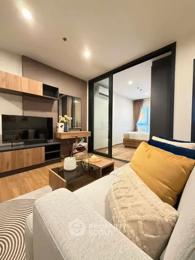 Modern living room with cozy sofa and stylish decor, open view to bedroom through sliding glass doors.