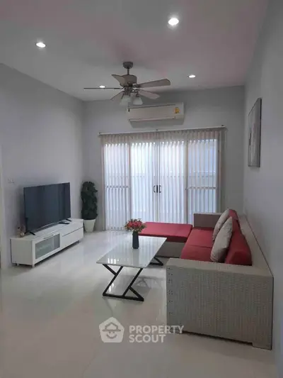 Modern living room with red sofa, sleek TV unit, and ceiling fan, featuring bright natural light from large windows.