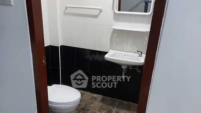 Compact bathroom with white sink and toilet, featuring black and white tiles.