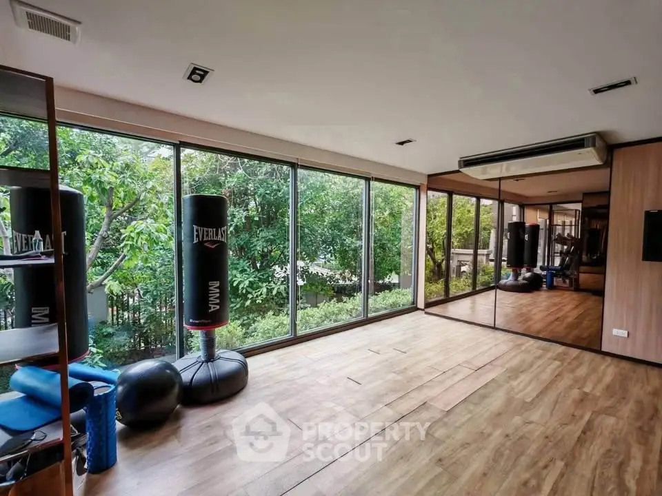Spacious home gym with floor-to-ceiling windows and lush garden view.
