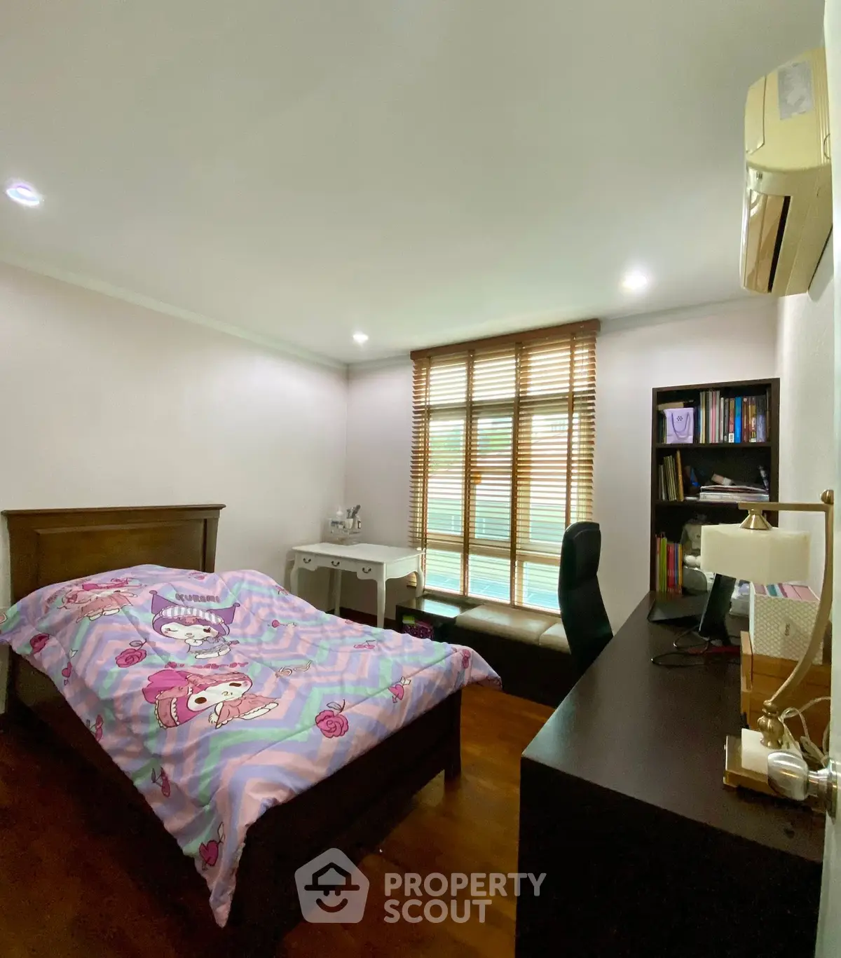 Cozy bedroom with wooden flooring, desk, and large window with blinds.