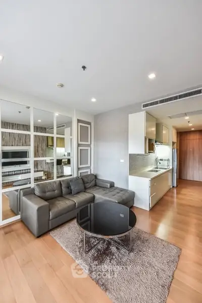 Modern living room with sleek kitchen in open layout, featuring stylish furniture and wooden flooring.