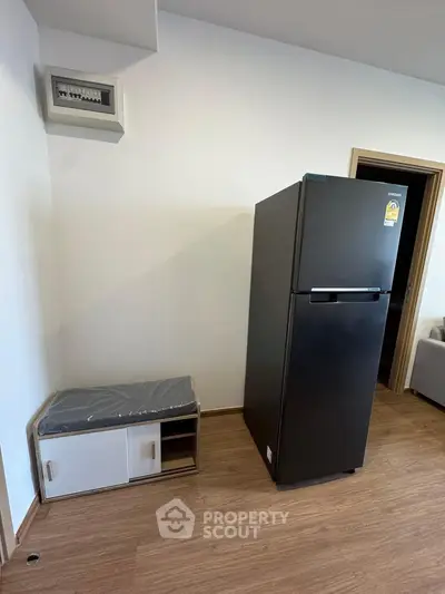 Modern apartment interior with sleek black fridge and compact storage unit on wooden flooring.