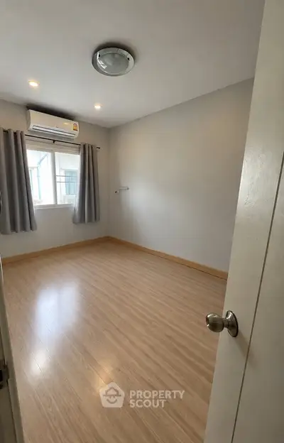 Spacious empty bedroom with wooden flooring and air conditioning, ready for customization.