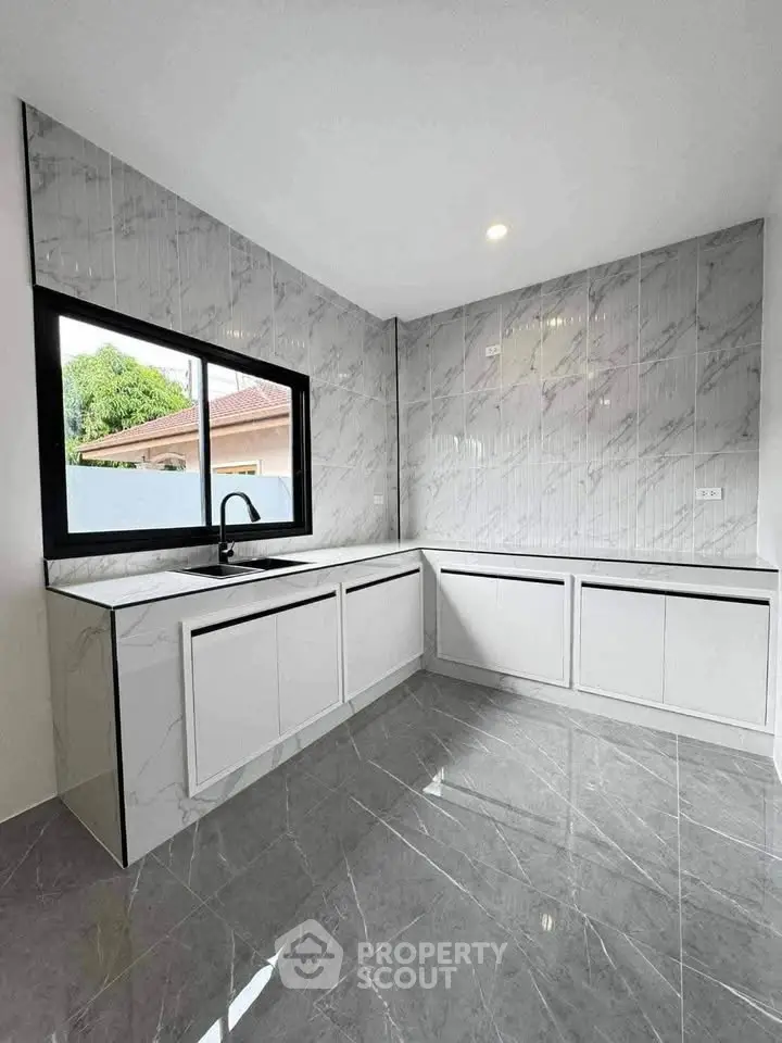 Modern kitchen with sleek marble countertops and large window for natural light.