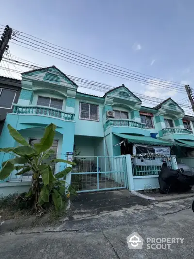 Charming turquoise townhouse with balcony and gated entrance in a serene neighborhood.