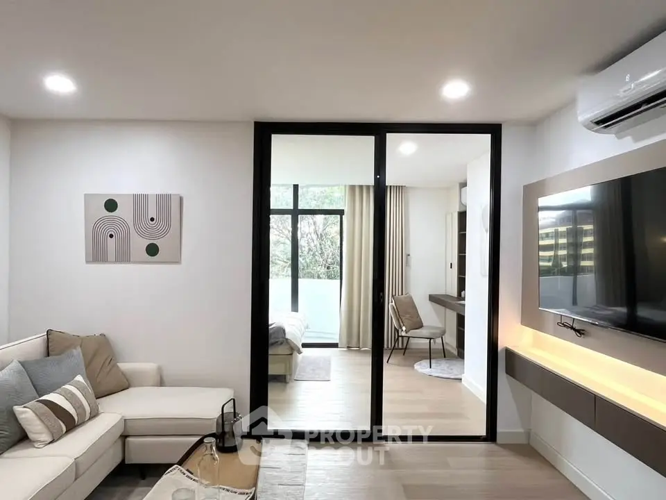 Modern living room with sliding glass doors leading to a cozy bedroom, featuring stylish decor and natural light.