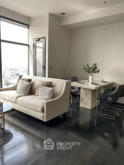 Modern living room with elegant sofa and dining area, featuring large windows and stylish decor.