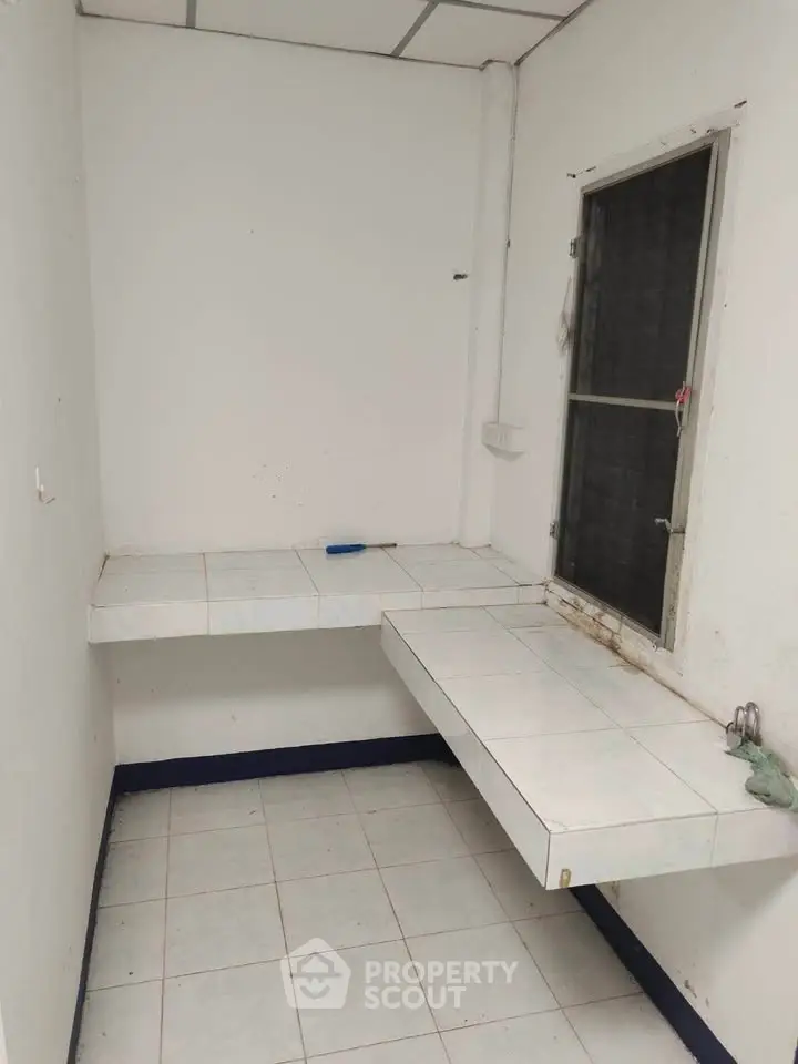 Compact utility room with tiled countertops and window, ideal for storage or small workspace.