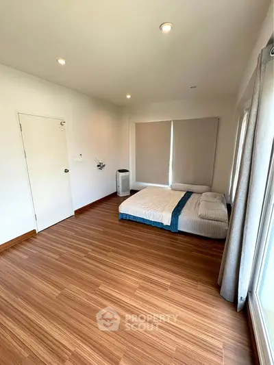 Spacious bedroom with wooden flooring and large windows for natural light.