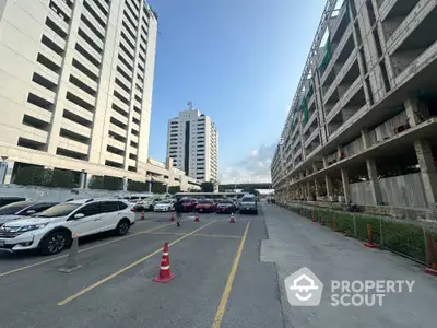 Expansive urban parking area flanked by high-rise buildings under a clear blue sky, showcasing the convenience of city living with ample parking space.