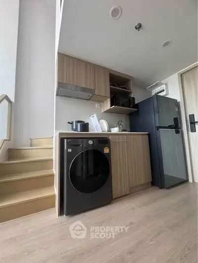 Modern kitchen with wooden cabinets, washing machine, and black fridge in a stylish apartment.