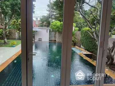 Luxurious private pool view from modern glass doors in serene garden setting.