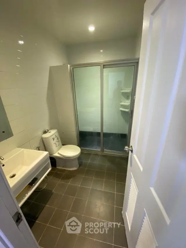 Modern bathroom with sleek fixtures, including a glass-enclosed shower and a white pedestal sink, complemented by dark floor tiles.