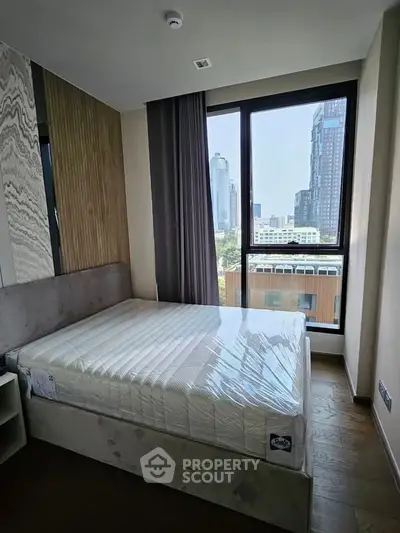 Modern bedroom with large window offering city view, featuring a new mattress and stylish decor.