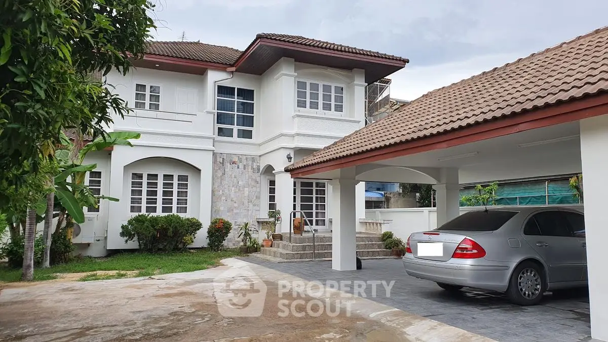 Elegant two-story house with carport and lush garden in suburban setting.