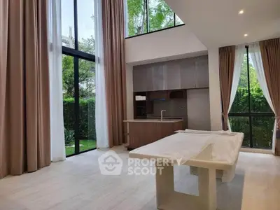 Spacious modern living room with high ceilings and large windows overlooking a lush garden.
