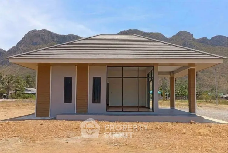 Modern single-story house with mountain backdrop, featuring large windows and a minimalist design.