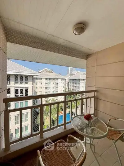 Charming balcony with seating overlooking a scenic residential complex and pool view.