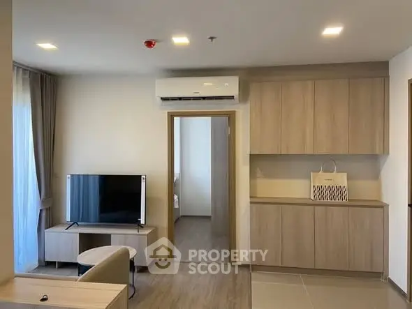 Modern living room with sleek cabinetry and wall-mounted TV, featuring neutral tones and ample natural light.