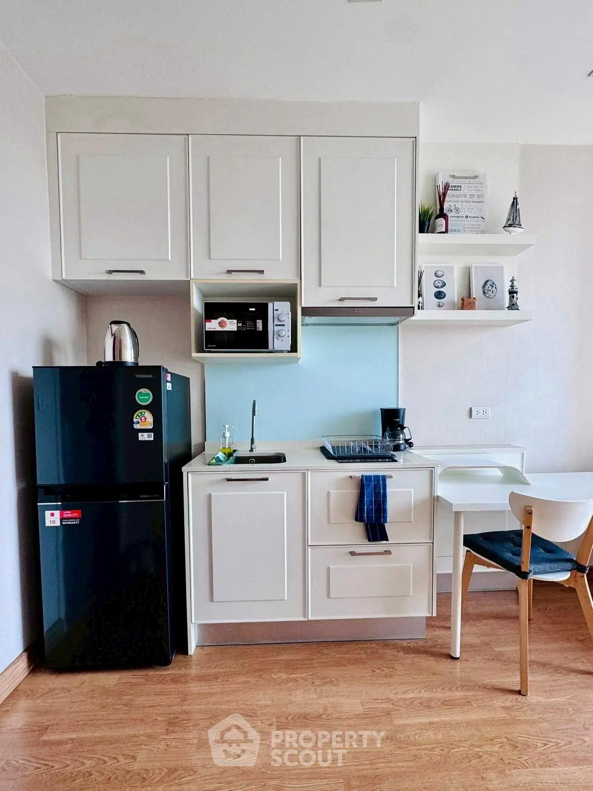 Modern compact kitchen with sleek white cabinets and black fridge in cozy apartment.