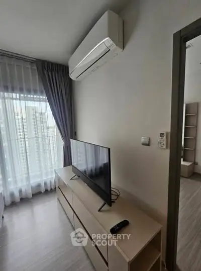 Modern living room with sleek TV setup and large window view in urban apartment.