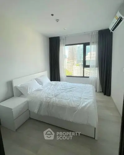 Modern bedroom with city view, featuring a cozy bed and large window for natural light.