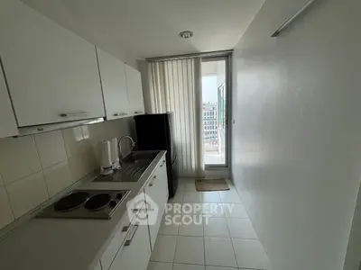 Compact kitchen with white cabinets and balcony access in modern apartment.