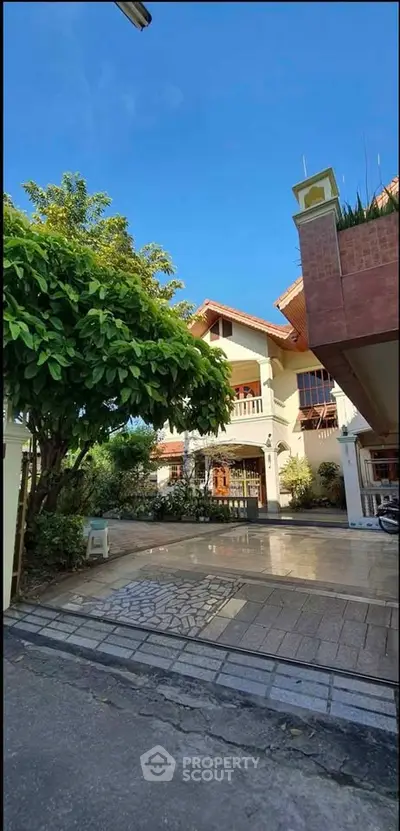 Charming two-story house with lush garden and spacious driveway under clear blue sky.