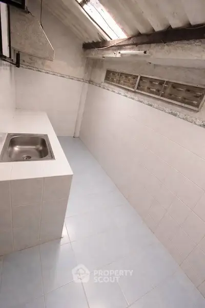 Compact kitchen space with tiled walls and skylight, featuring a single stainless steel sink.