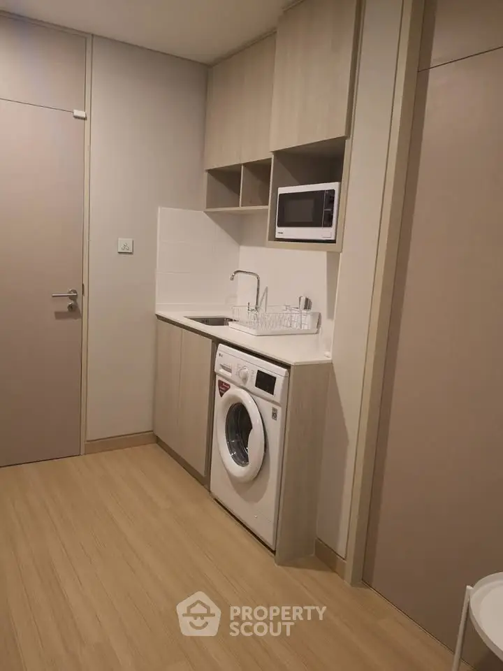 Modern compact kitchen with integrated washing machine and microwave in sleek cabinetry.