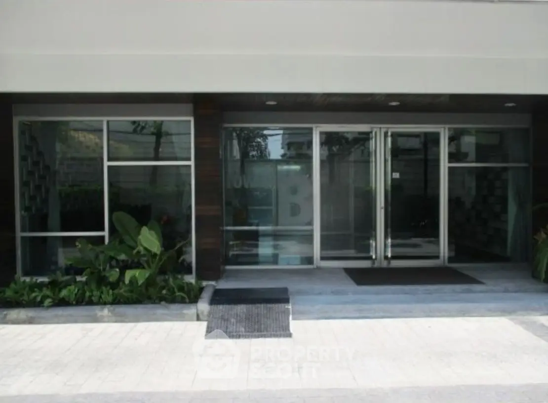 Modern building entrance with glass doors and lush greenery