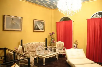Elegant living room with vintage furniture and chandelier, featuring vibrant red curtains and classic artwork.