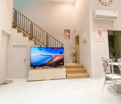 Spacious living room with modern decor and large TV, featuring elegant staircase and stylish furniture.
