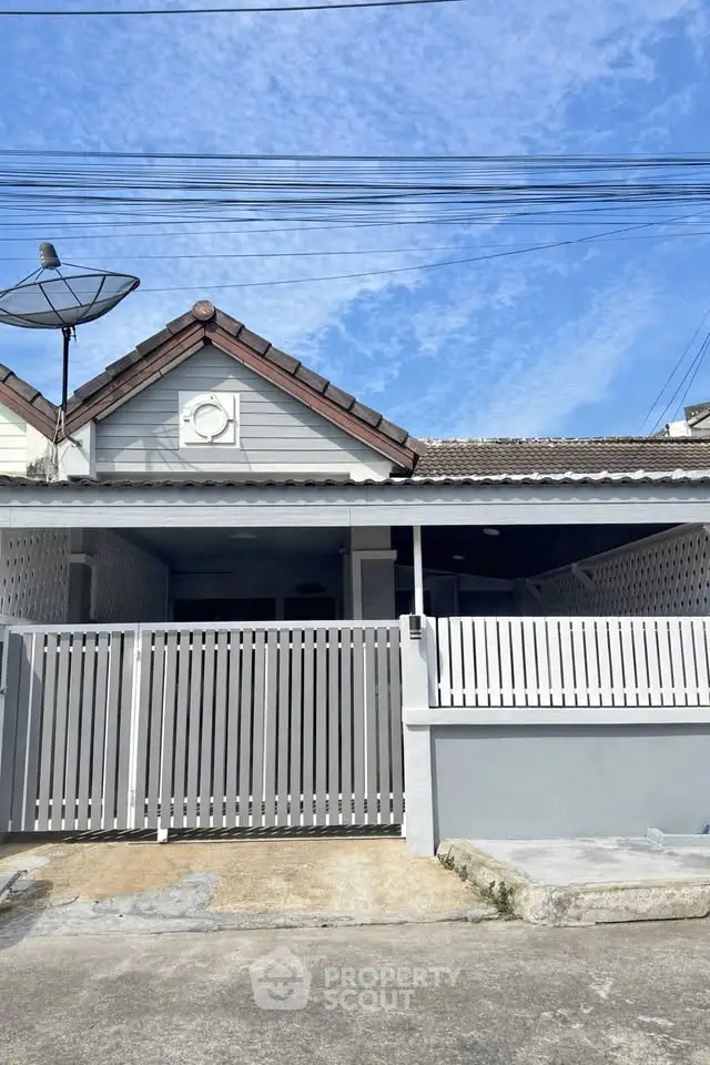 Charming single-story home with gated entrance and satellite dish under a clear blue sky.