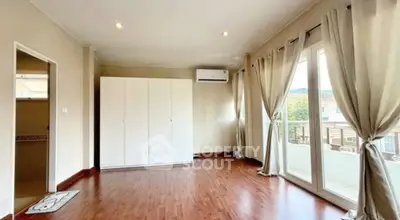 Spacious bedroom with large windows and balcony access, featuring wooden flooring and neutral decor.