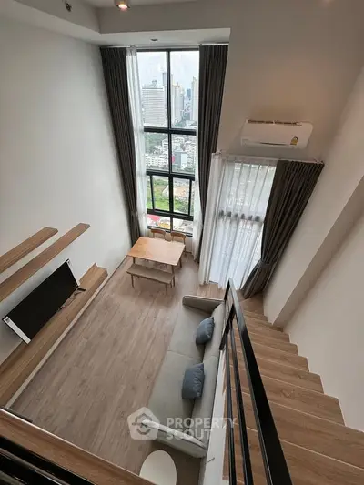 Modern loft apartment with high ceilings and large windows offering city views, featuring a cozy living area and stylish decor.