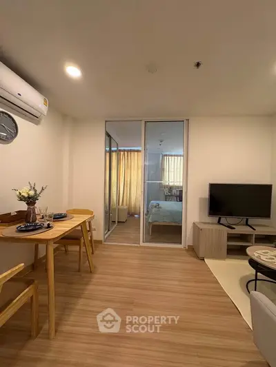 Modern living room with wooden flooring, dining set, and view into cozy bedroom