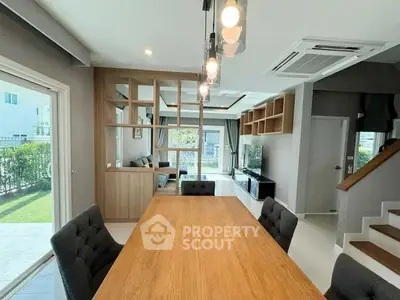 Modern living room with wooden dining table and large windows offering garden view.