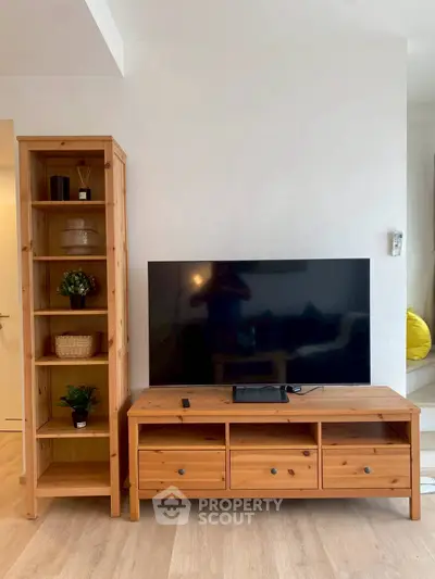 Modern living room with wooden TV stand and shelving unit, featuring a sleek flat-screen TV.