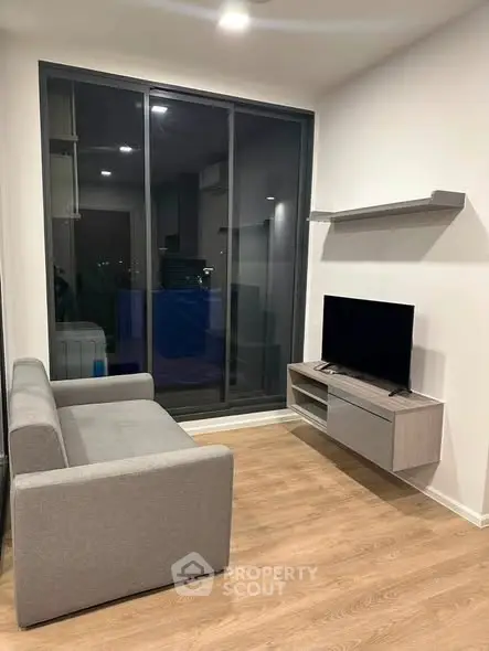 Modern living room with sleek furniture and large window offering city views.