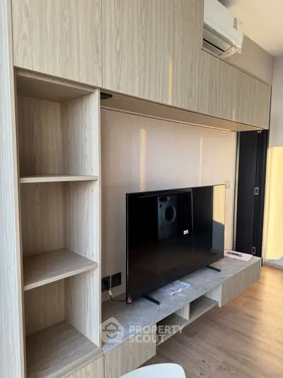 Modern living room with sleek wooden cabinetry and mounted TV, featuring contemporary design and natural light.