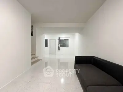 Spacious minimalist living room with sleek black sofa and white walls, perfect for modern living.