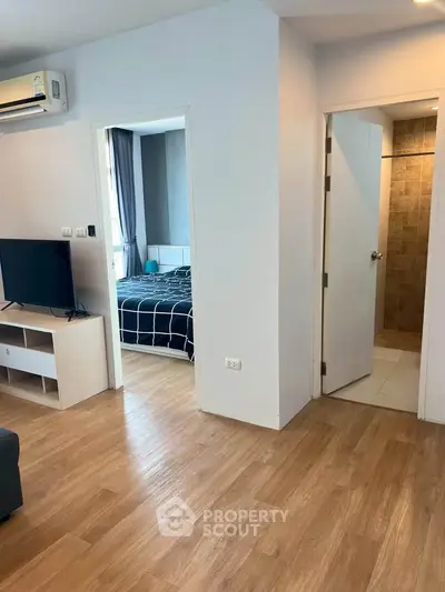 Modern apartment interior with wooden flooring, featuring a cozy living area and a glimpse into a stylish bedroom.