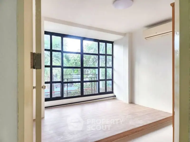 Bright room with large windows and wooden flooring, perfect for a cozy living space.