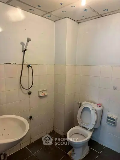 Basic bathroom with shower, toilet, and sink in a tiled setting.